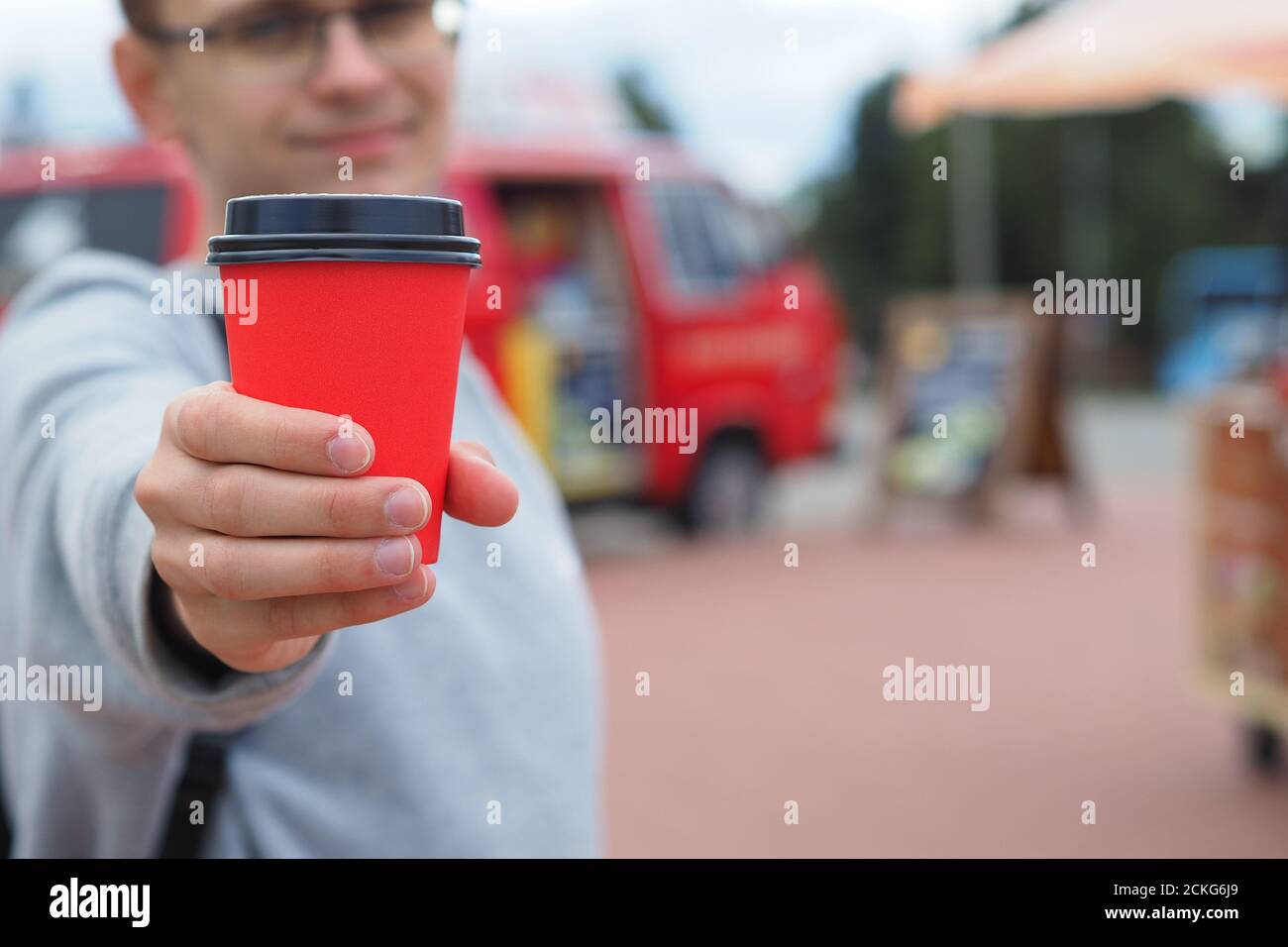 Einwegglas mit einem Getränk in der Hand eines Junger lächelnder Mann Stockfoto