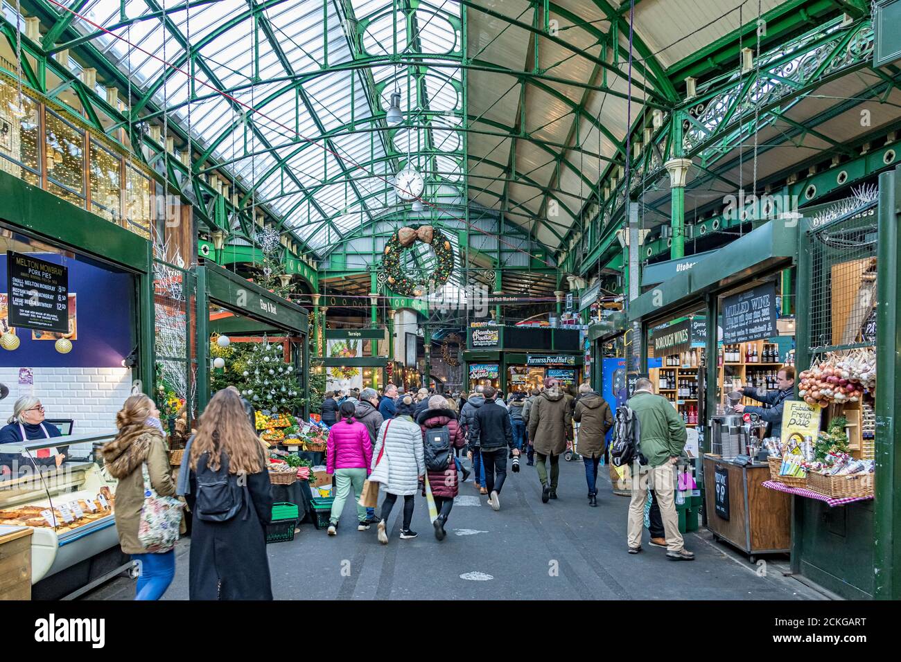Leute, die einkaufen und bummeln gehen an den Marktständen unter dem Glas- und Schmiedeeisendach am Borough Market, Southwark, London Stockfoto