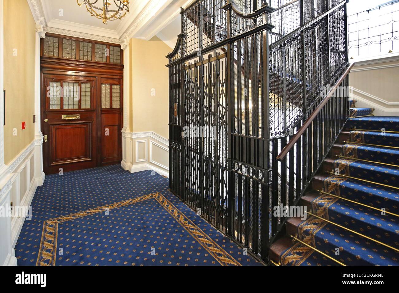 Ein traditioneller Metallaufzug im Treppenhaus eines Londoner Wohnblocks. Neu renoviert, zeigt neuen Teppich, Treppengeländer und kunstvolle Türen Stockfoto