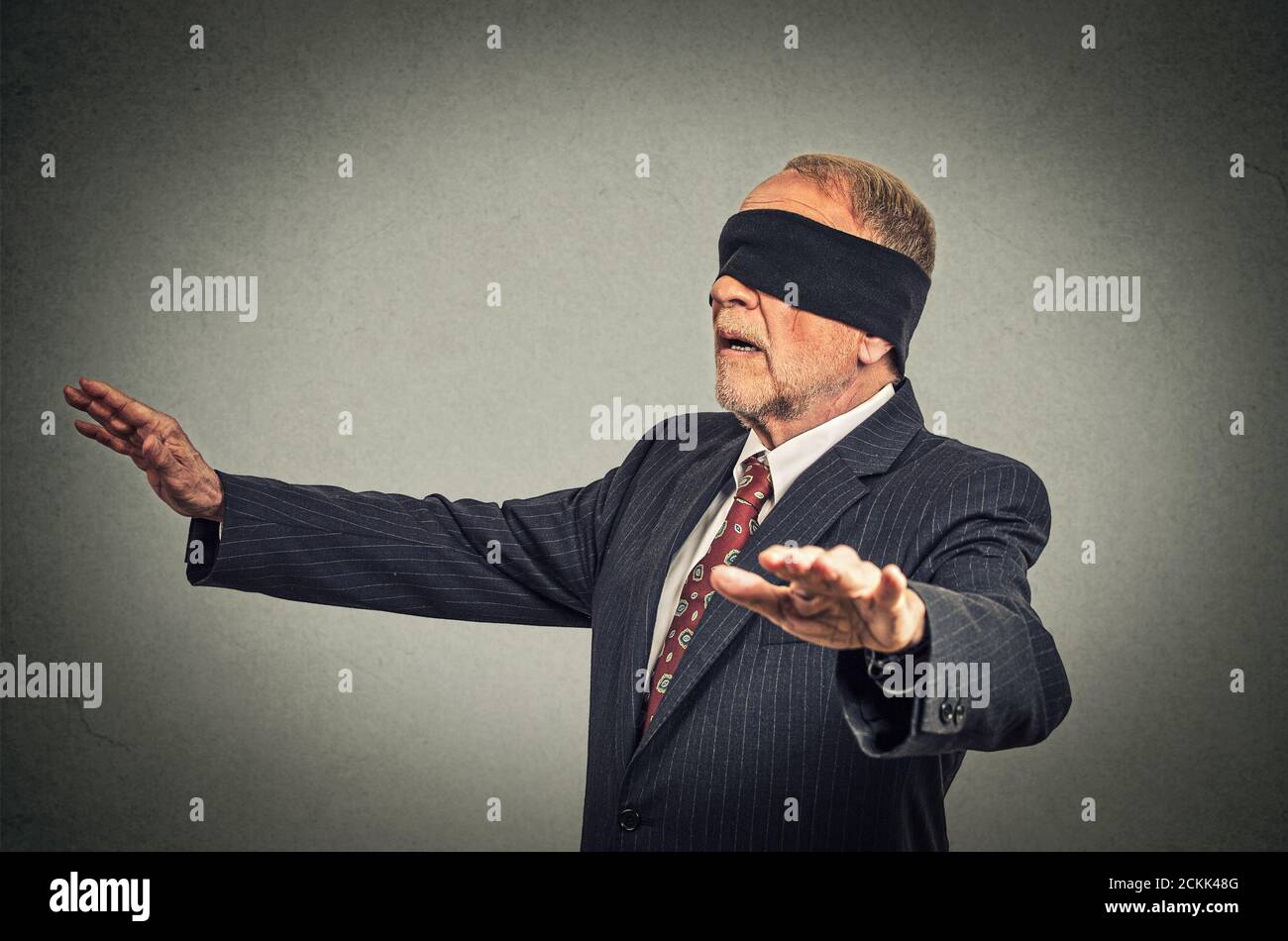 Portrait Senior Business Mann in Anzug mit verbundenen Augen strecken seine Arme Draußen isoliert auf grauem Wandhintergrund Stockfoto