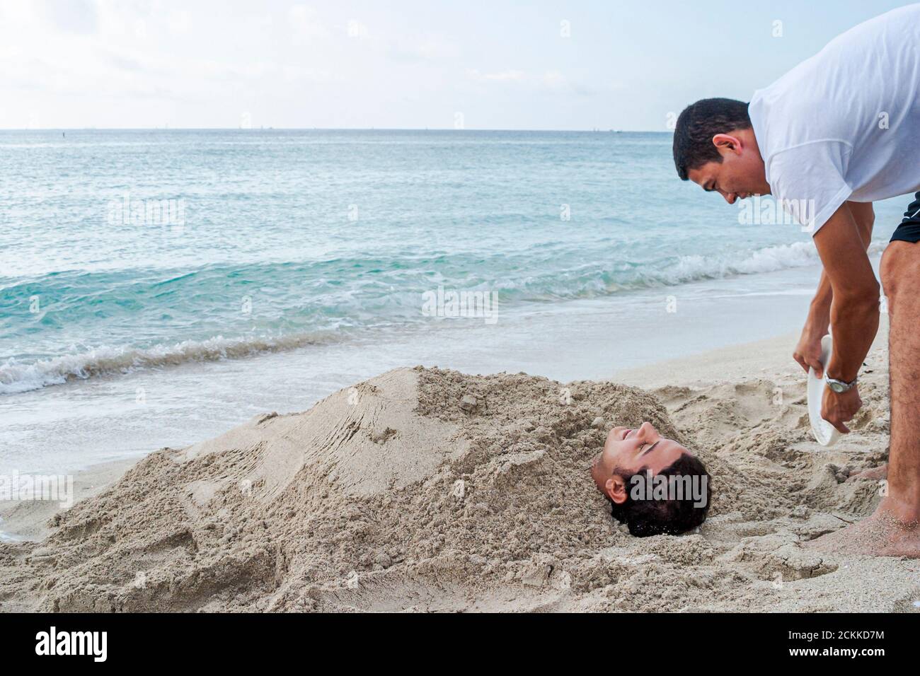 Miami Beach, Florida, Atlantikküste, Küste, Hispanic, Erwachsene Erwachsene Männer Männer, vergraben Sand durch Wassersurf, Teenager Teenager Stockfoto