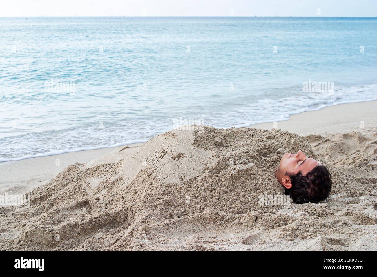 Miami Beach, Florida, Atlantikküste, Küste am Meer, hispanischer Junge, Mann, vergrabener Sand durch Wassersurf, Teenager im Teenageralter Stockfoto