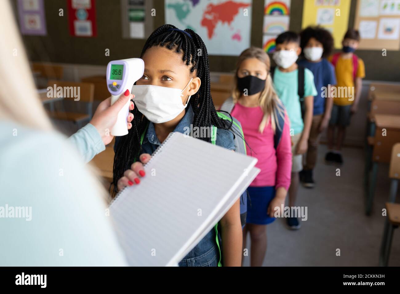 Mädchen tragen Gesichtsmaske bekommen ihre Temperatur in der Klasse gemessen In der Schule Stockfoto
