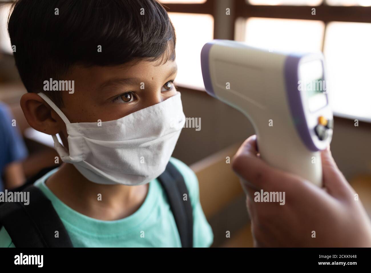 Junge trägt Gesichtsmaske bekommen seine Temperatur in der Klasse gemessen In der Schule Stockfoto
