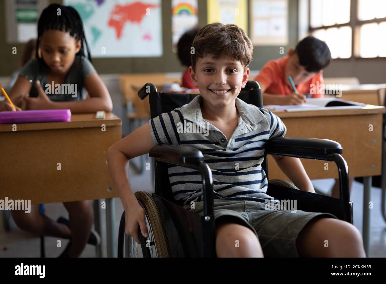 Porträt des behinderten Jungen lächelnd, während er in seinem Rollstuhl sitzt In der Schule Stockfoto