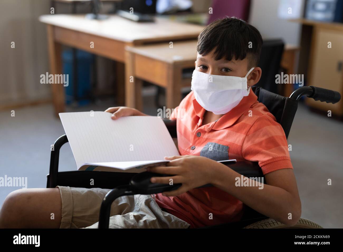 Porträt des Jungen deaktivieren trägt eine Gesichtsmaske sitzen in Sein Rollstuhl in der Schule Stockfoto