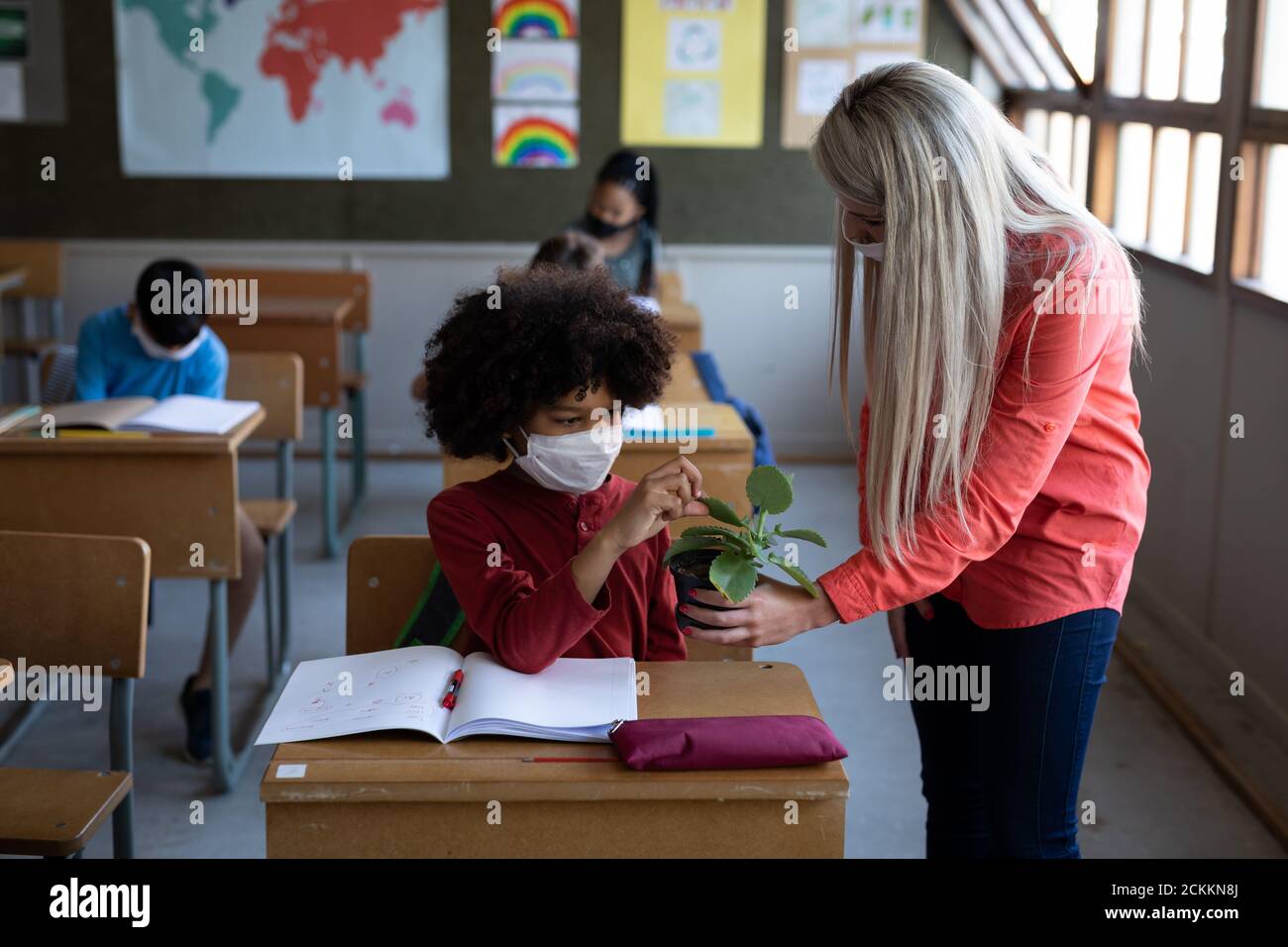 Weibliche Lehrerin trägt Gesichtsmaske zeigt einen Pflanzentopf zu Ein Junge in der Schule Stockfoto