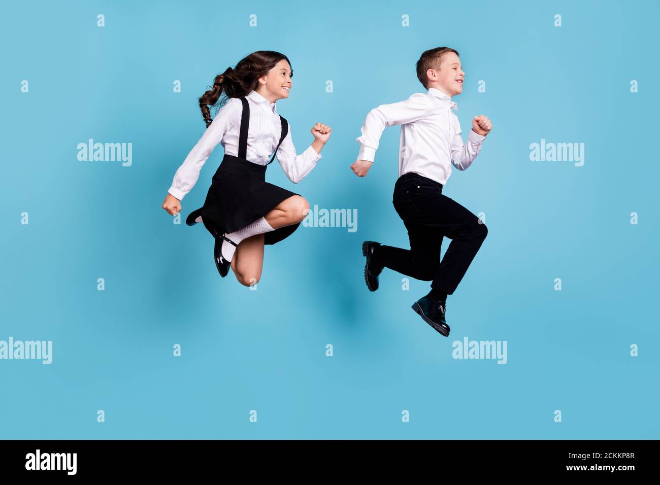 In voller Länge Profil Foto von zwei kleinen Mädchen junge Schulkinder Bruder Schwester Klassenkameraden springen glücklich laufen Schule Konzept tragen weiß hemd schwarze Hose Stockfoto