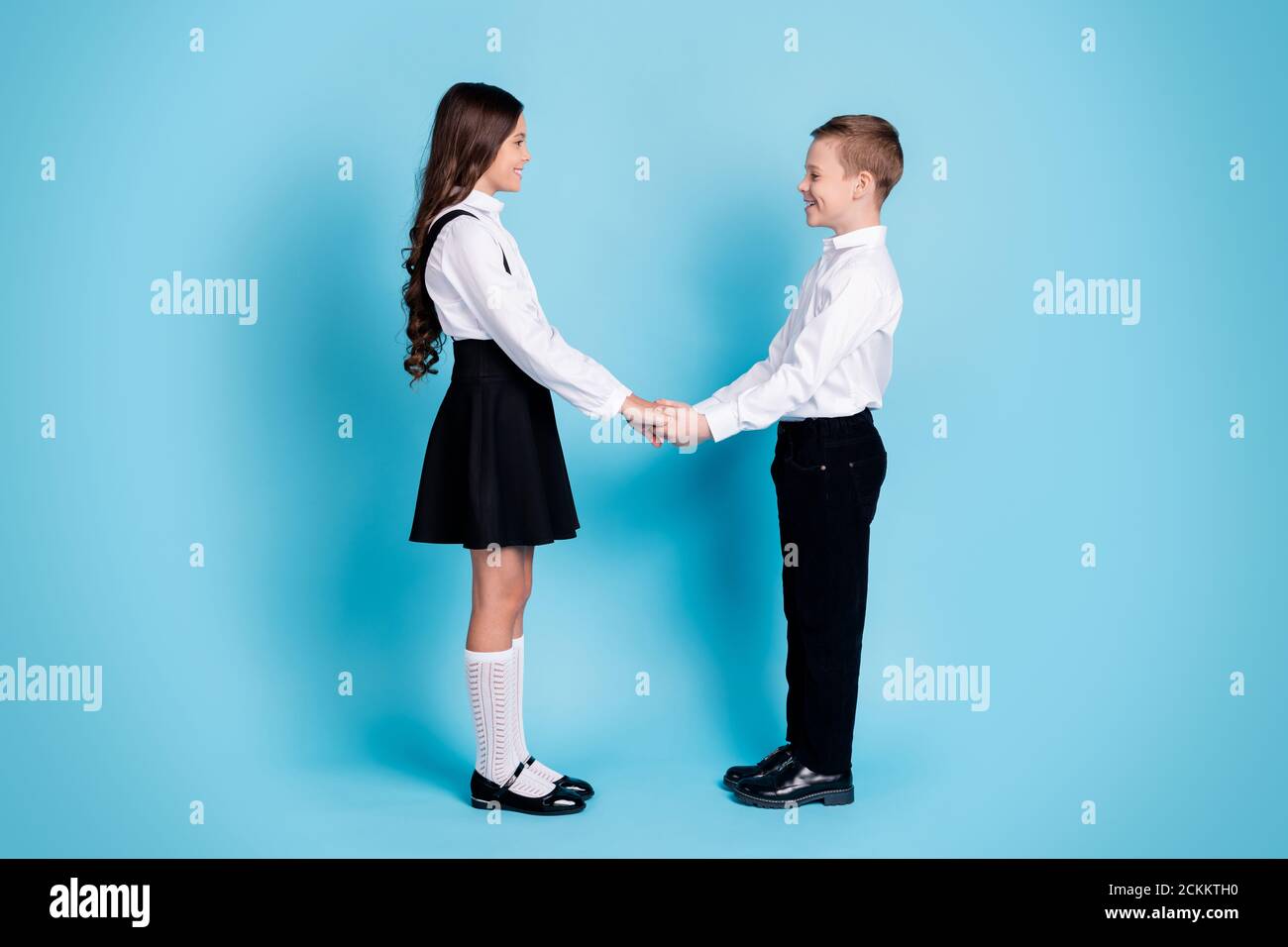 In voller Länge Profil Foto von zwei Mädchen junge Schulkinder glänzend Lächelnd halten Hände Blick Augen gegenüber vorbereiten Tanz tragen Uniform Weißes Hemd schwarz Stockfoto