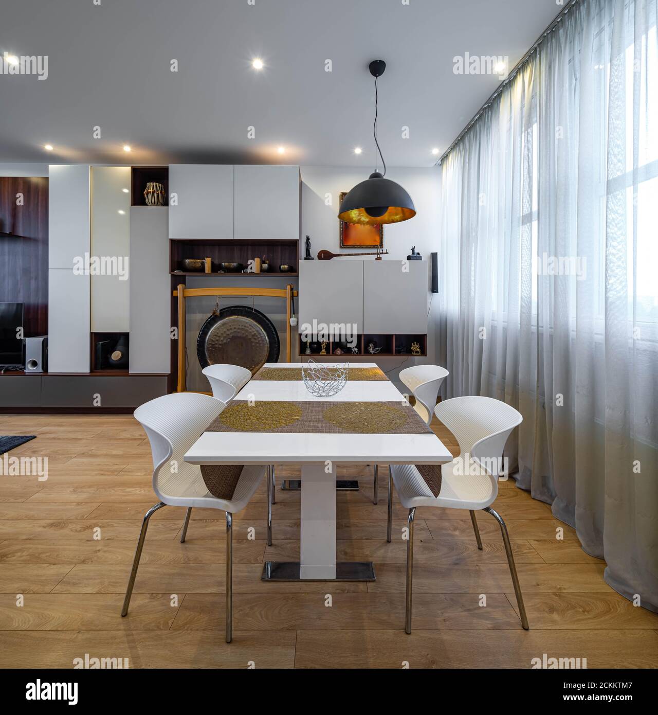 Modernes Interieur des Wohnzimmers in Luxus-Wohnung. Tisch und Stühle.  Inneneinrichtung. Tibetische Schalen und dekorative gong. Weiße Wandeinheit  Stockfotografie - Alamy