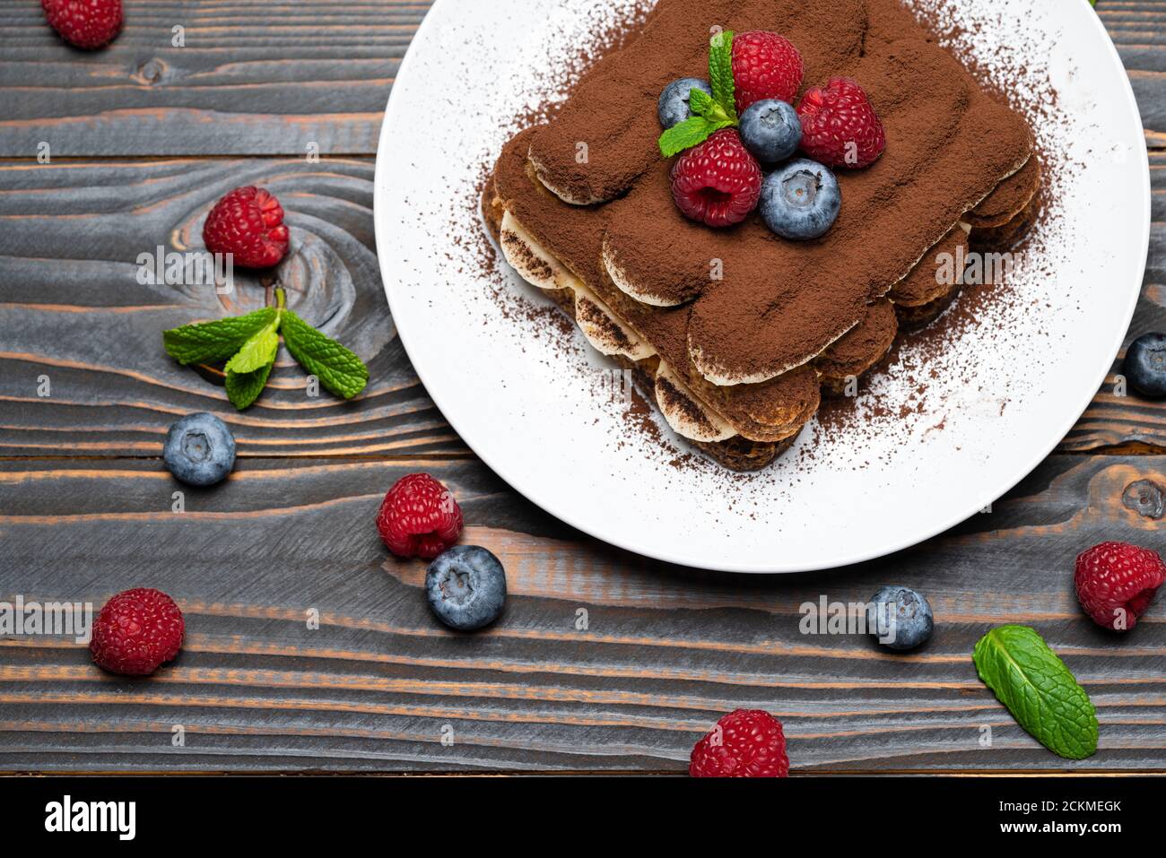 Portion Classic Tiramisu Dessert mit Himbeeren und Heidelbeeren auf Holzhintergrund Stockfoto