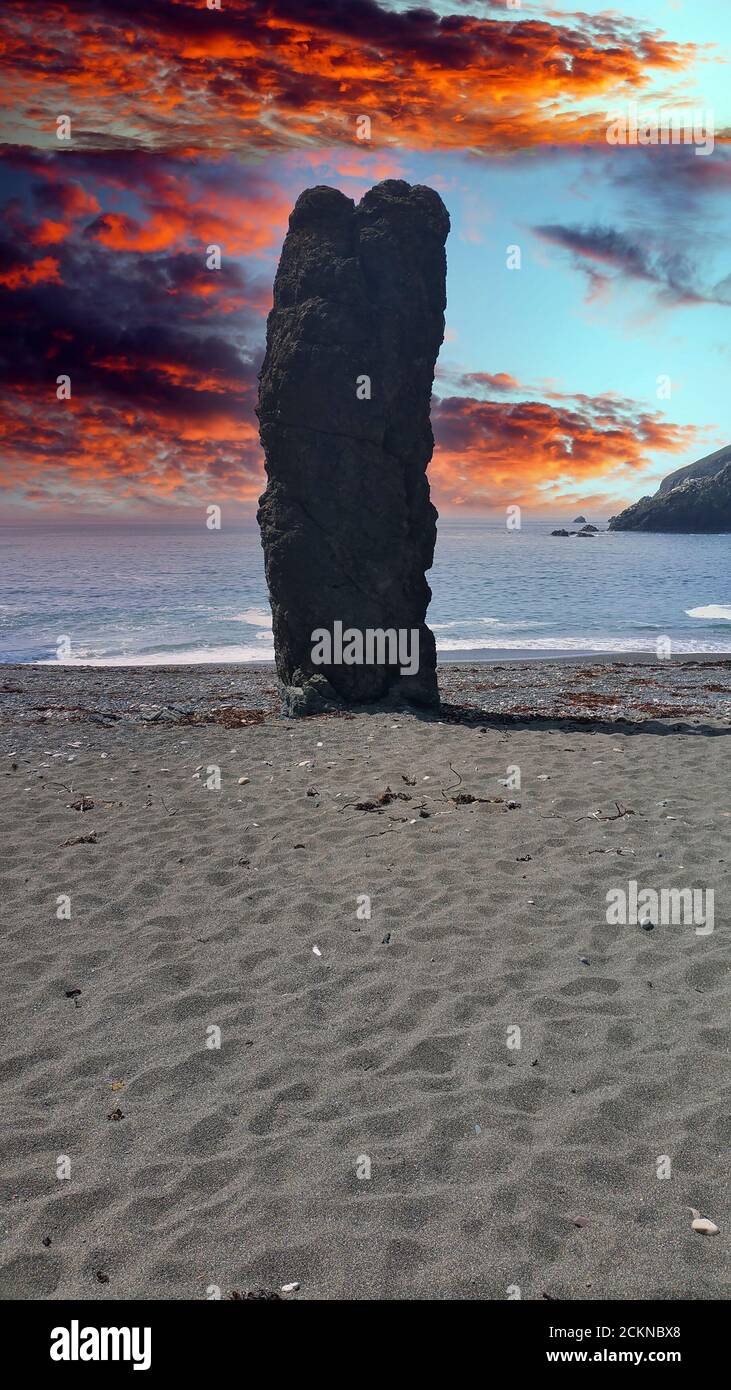 Einsamer Steinmonolith an einem abgelegenen Strand vor buntem Himmel. Stockfoto