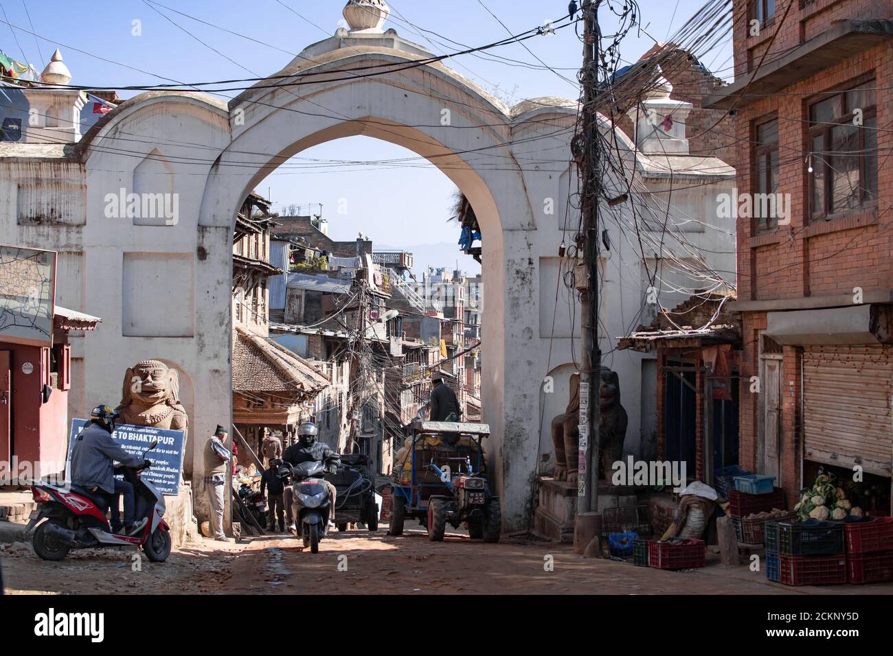 Bhaktapur, Kathmandu, Nepal - 23. Dezember 2019: Nicht identifizierte Menschen auf Motorrädern und einem Traktor fahren ein und aus einem weißen gewölbten Eingang Stockfoto