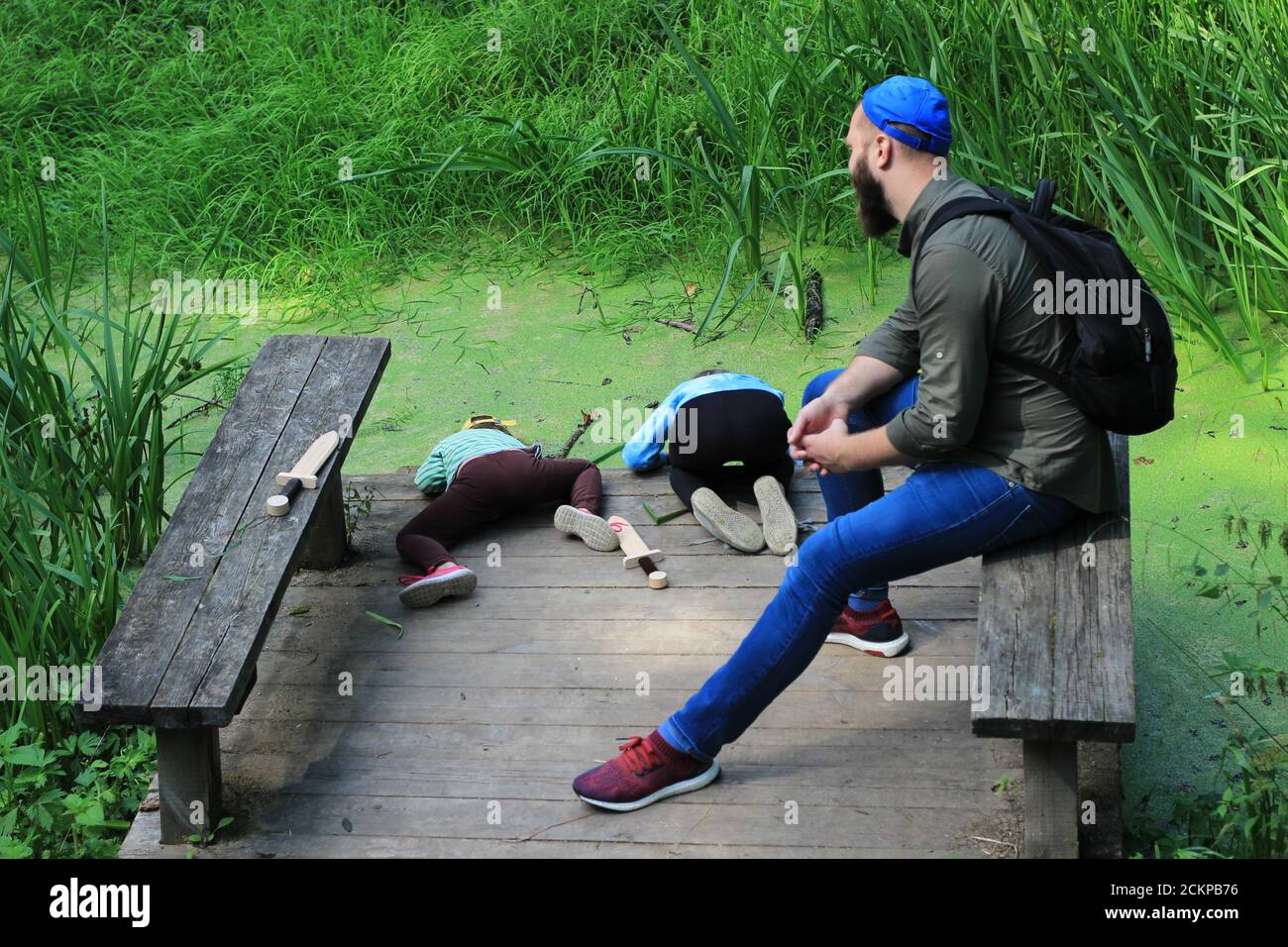 Ein Mann sitzt auf einer Bank und sieht Kinder an Wiedergabe Stockfoto
