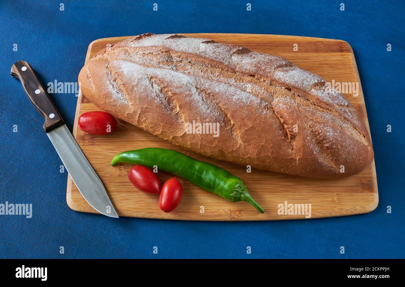 Brot, Tomaten, Chili und ein Messer liegen auf dem Schneidebrett, geringe Schärfentiefe, Stillleben Stockfoto