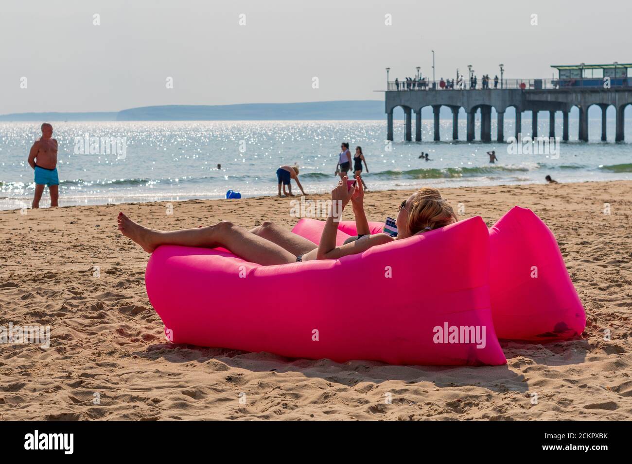 Boscombe, Bournemouth, Dorset, UK, 16. September 2020, Wetter. Menschen am Strand und im Meer genießen den dritten Tag der September Hitzewelle mit heißem Sonnenschein am Nachmittag. Eine Frau entspannt sich in einer großen aufblasbaren rosa Sonnenliege. Kredit: Paul Biggins/Alamy Live Nachrichten Stockfoto