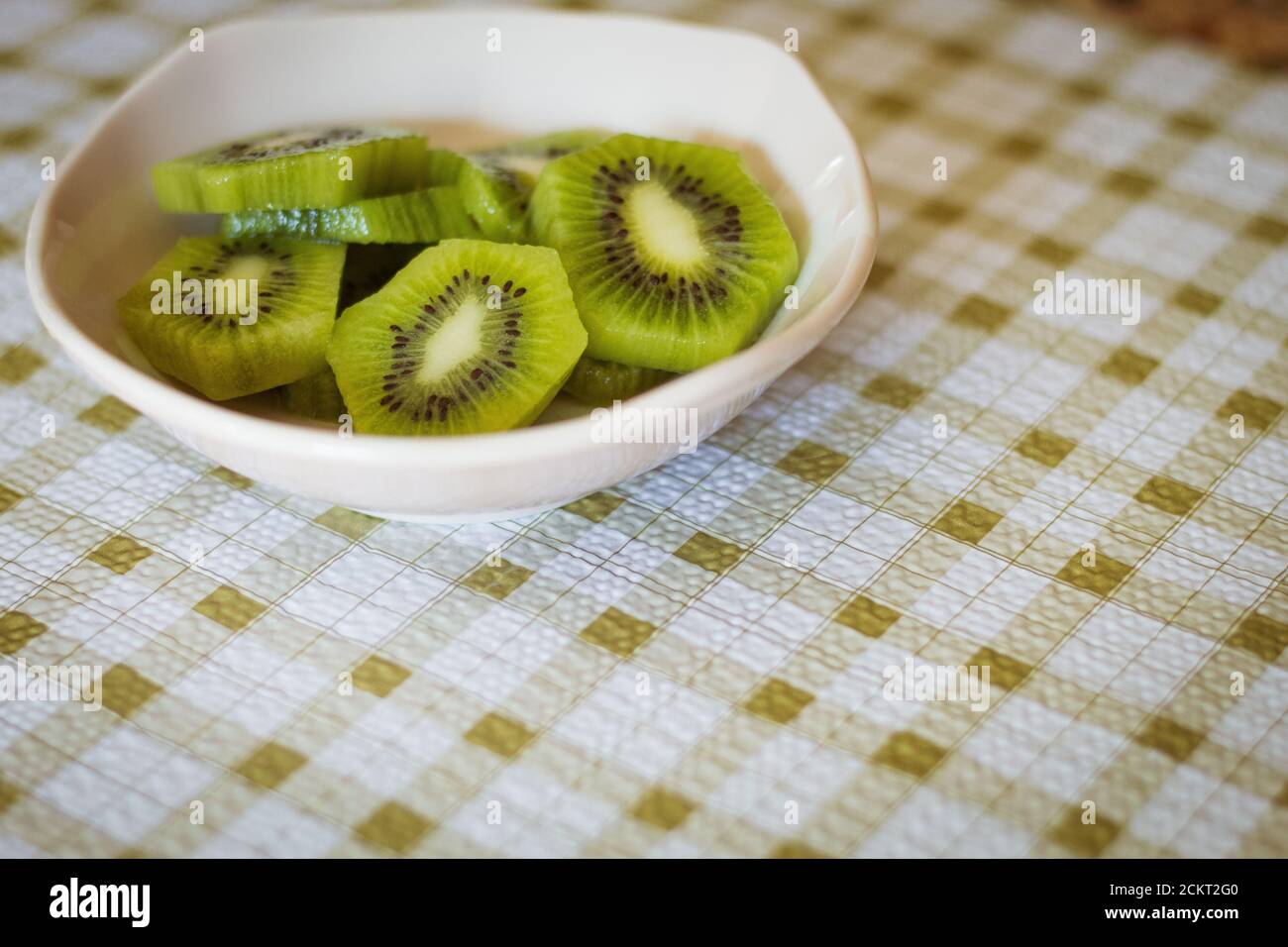 Kiwi in Scheiben geschnitten in einer rosa Schale auf karierter grüner Tischdecke Stockfoto