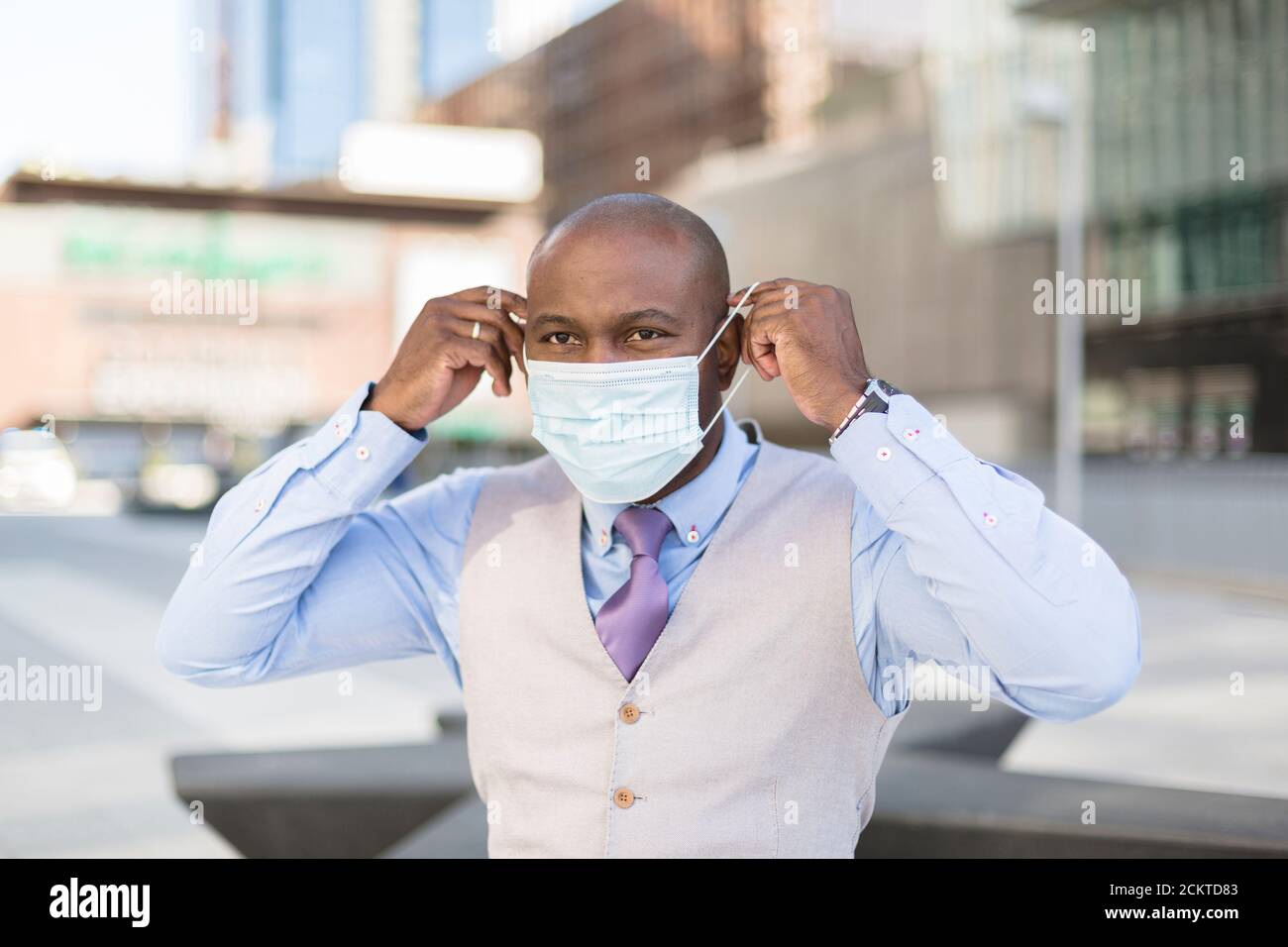 Porträt eines schwarzen Mannes, der eine medizinische Maske auf sein Gesicht legt. Er ist draußen in der Stadt. Konzept der neuen Normalität. Stockfoto