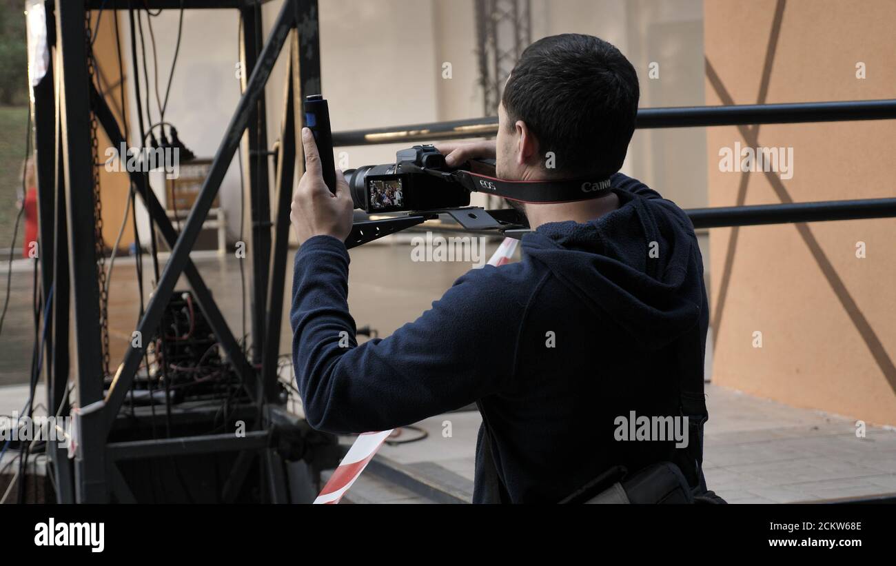 Ein männlicher Videofilmer nimmt Videos auf einer DSLR-Kamera auf. Die Aufnahmen werden bei Tageslicht in 4K aufgenommen Stockfoto