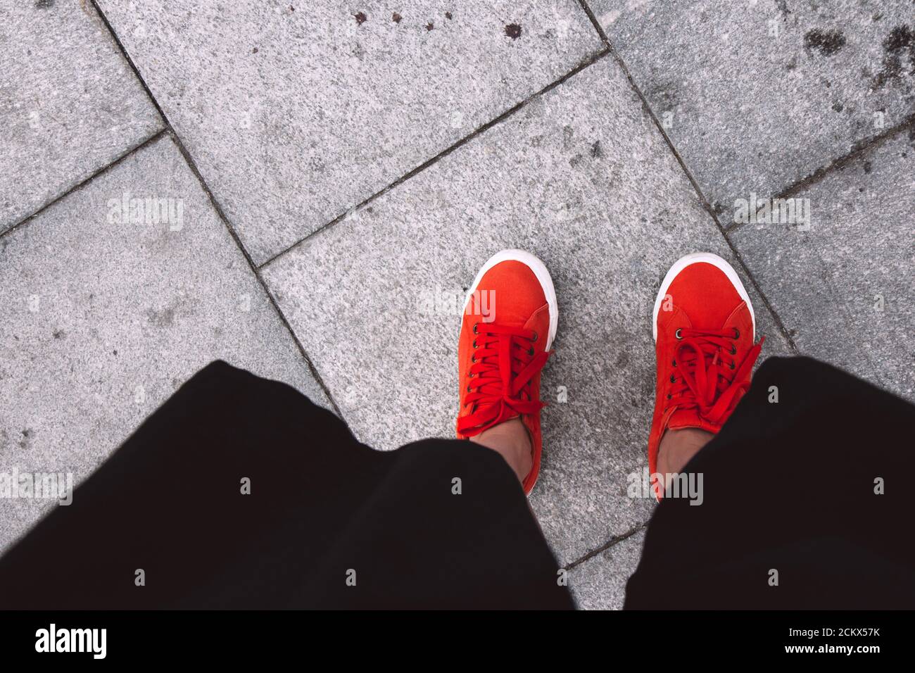 Weibliche Füße von oben gesehen. Selfie für jeden Einsatz. Fuß und Beine in roten Sneakers. Fuß steht auf den grauen Fliesen. Mit Kopierbereich. Füße draußen Stockfoto