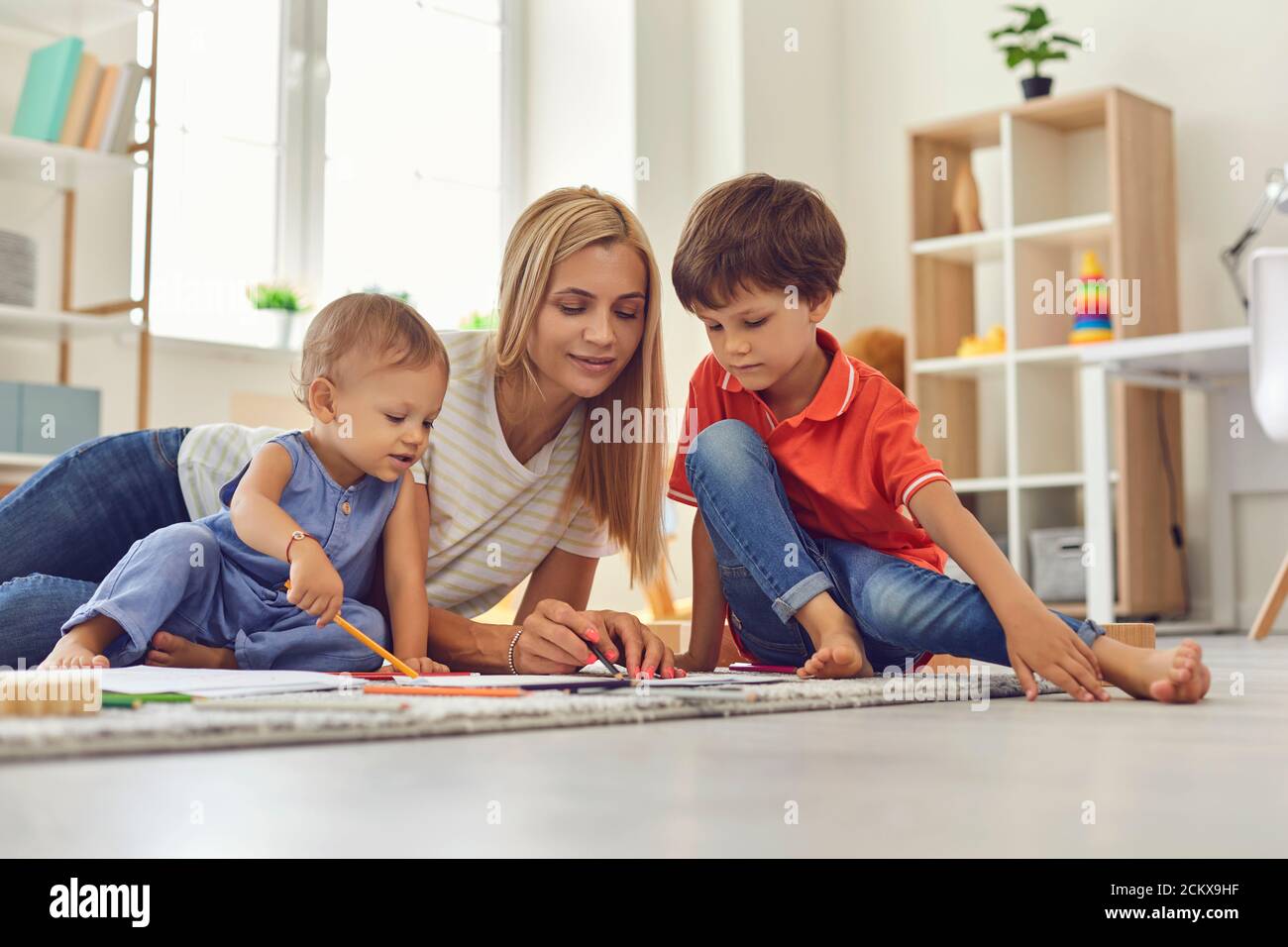 Junge Mama und Kinder zeichnen Bild zusammen sitzen auf dem Boden Im Kinderzimmer Stockfoto