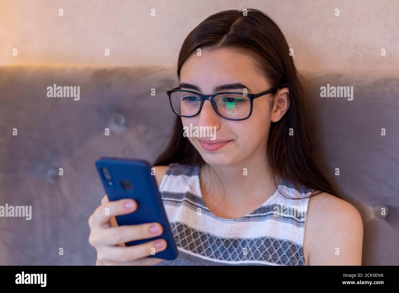 Junge kaukasische Mädchen mit Brille sitzen Rest auf dem Sofa und Surfen im Internet auf Handy, Millennial weiblich in Brille SMS-Messaging auf Smartphone Stockfoto