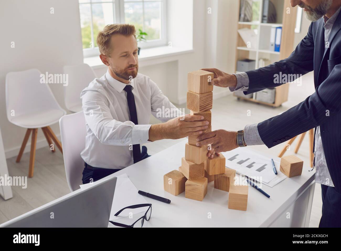 Unternehmer verschiedener Generationen bauen Turm zusammen als Metapher für Geschäftsnachfolge Stockfoto