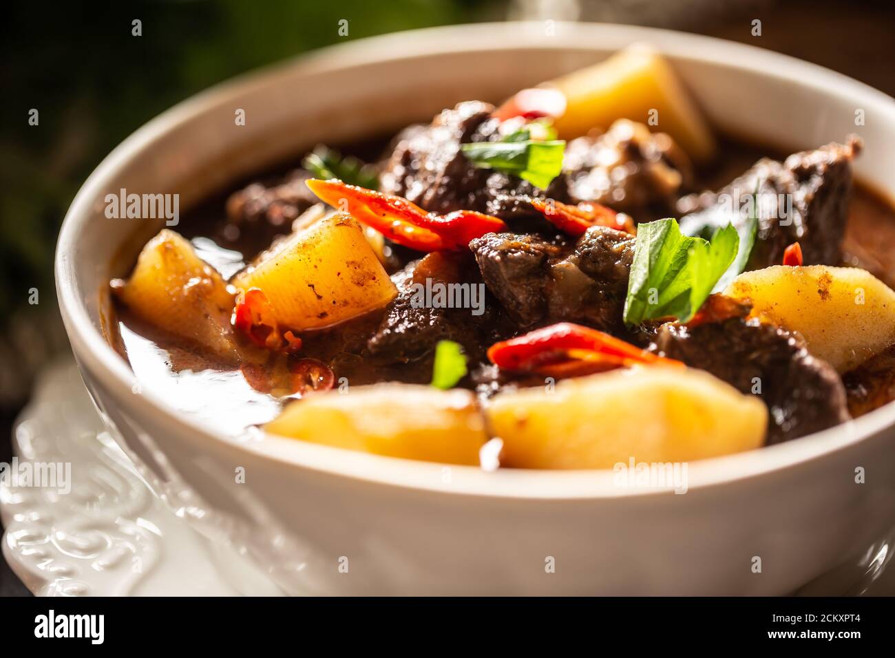 Schüssel Gulasch mit Fleisch, Kartoffeln, Chilis und Petersilie Stockfoto