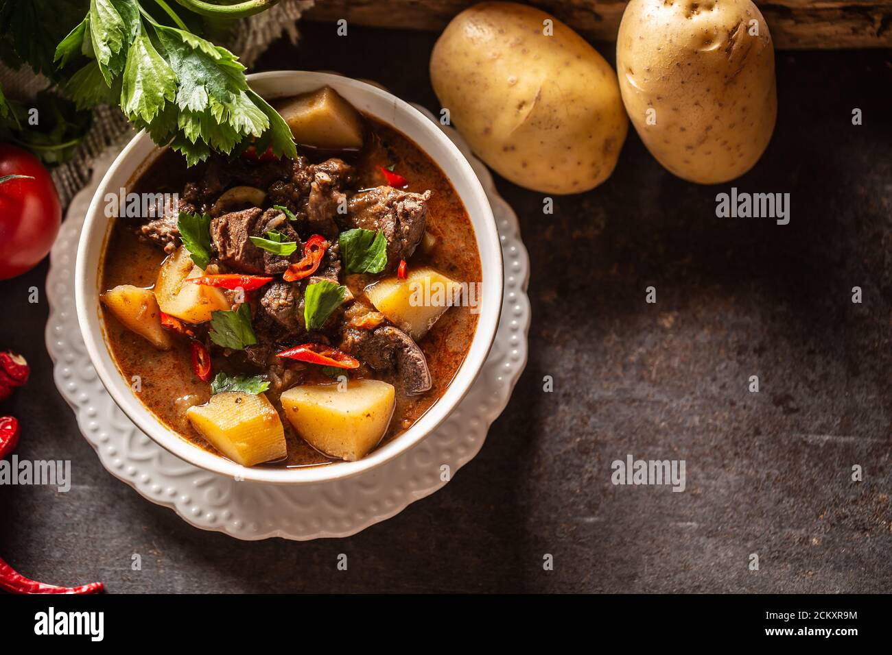 Schüssel Gulasch mit Fleisch, Kartoffeln, Chilis und Petersilie Stockfoto