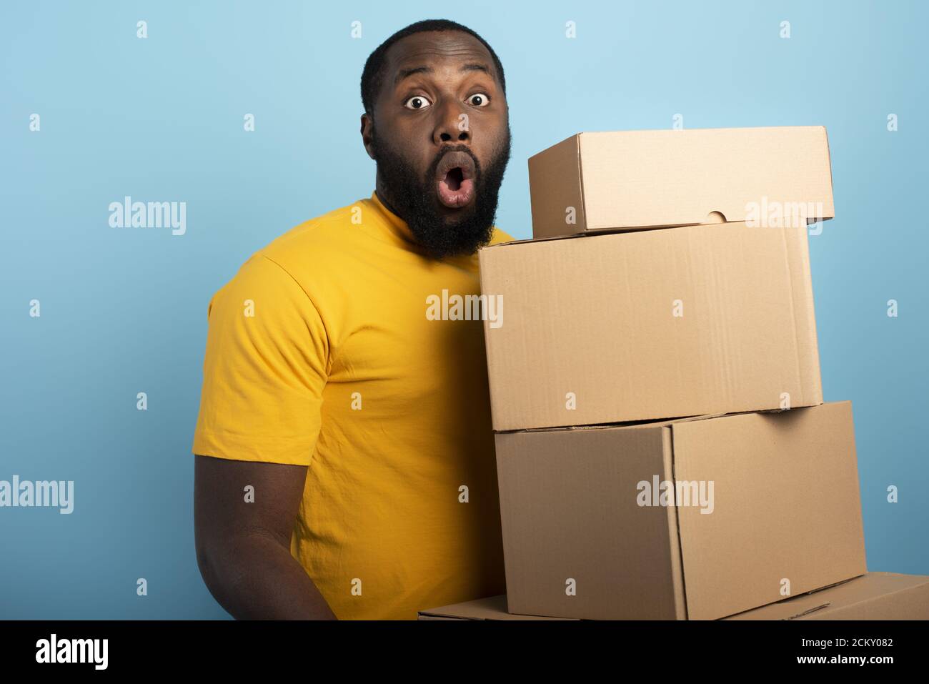 Überrascht Mann hält eine Menge von empfangenen Paketen. Cyanfarbener Hintergrund Stockfoto