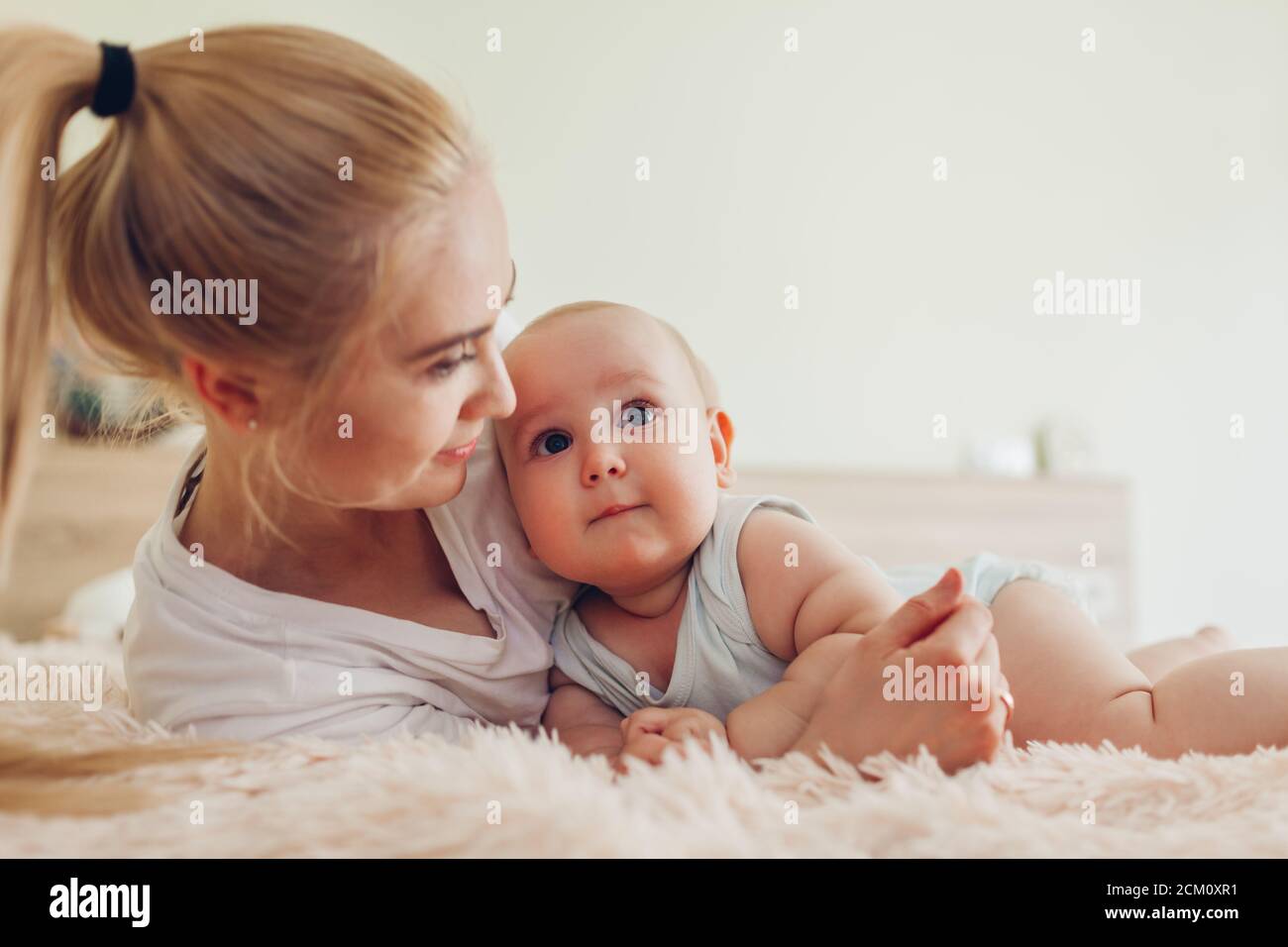 Frau, die mit ihrem Baby auf dem Bett liegt. Mutter umarmt Kind. Familie zu Hause entspannen Stockfoto