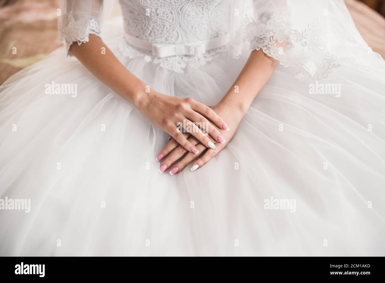 Die weiblichen Hände der hellhäutigen Braut liegen auf dem Weißes Hochzeitskleid Stockfoto