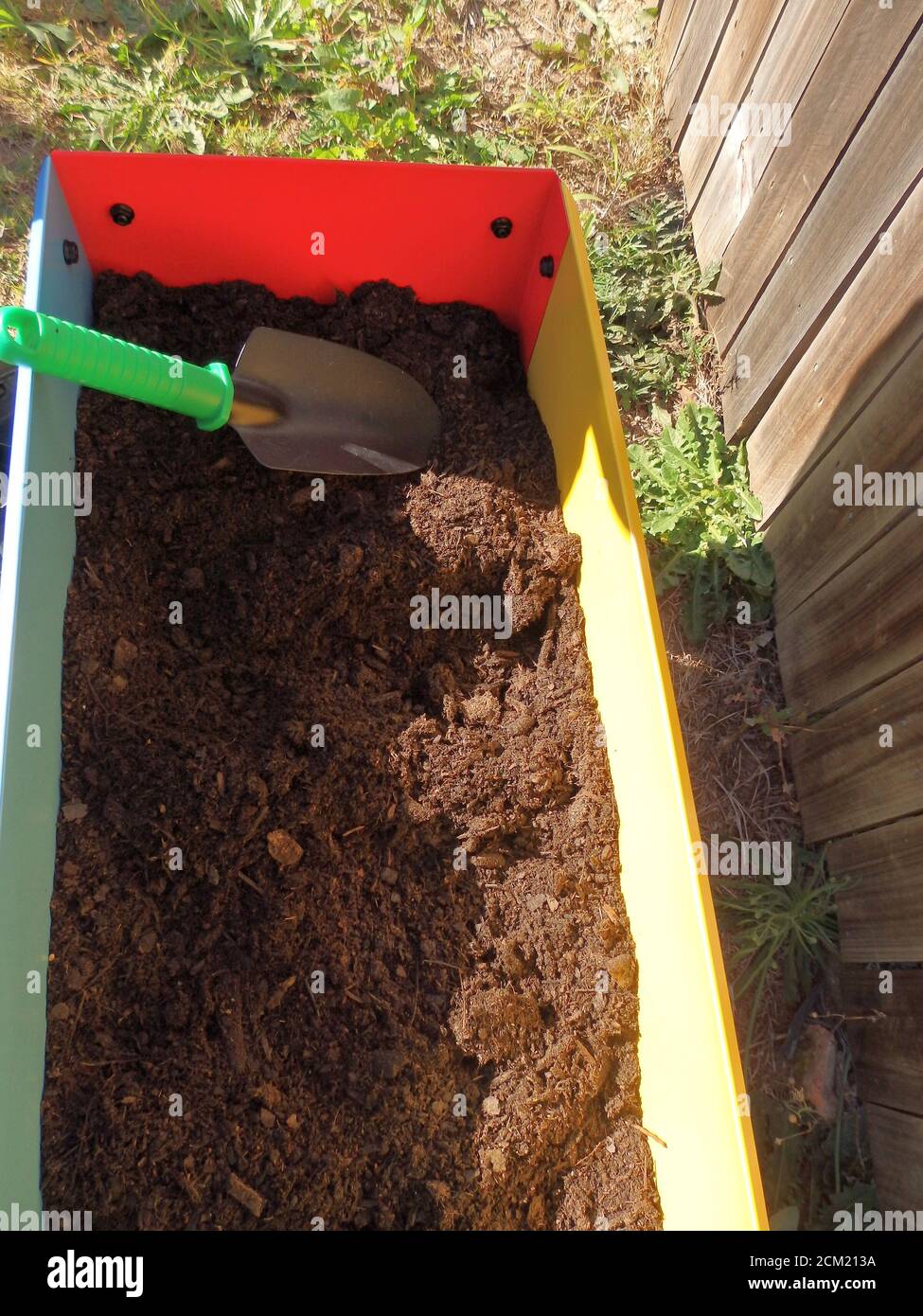 Eine Kinderplantschachtel gefüllt mit Erde und Gartenkelle. Stockfoto