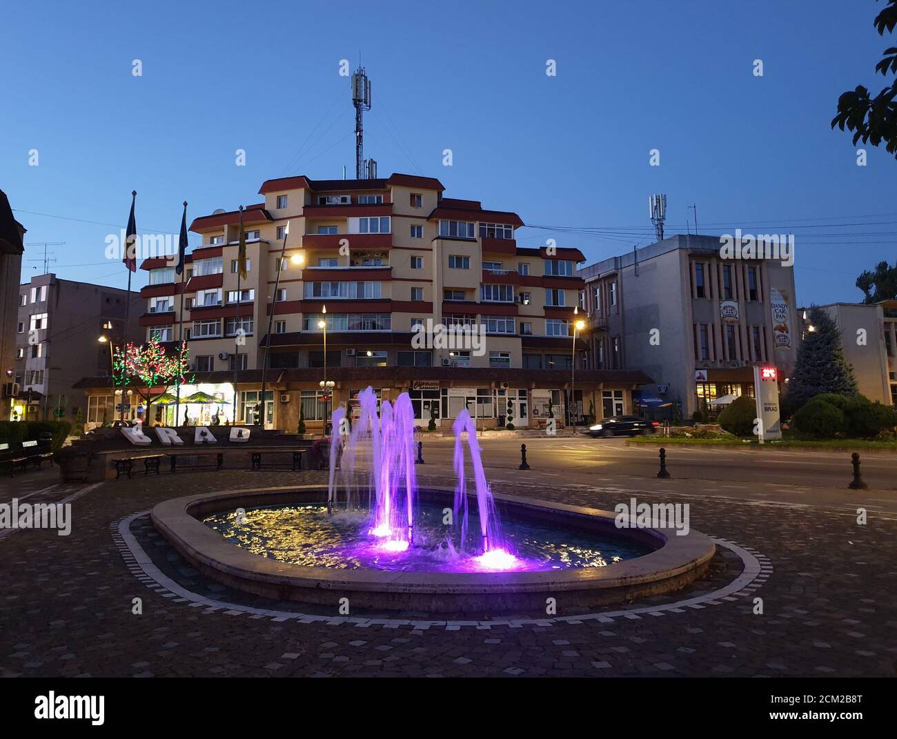 Brad Stadtzentrum Brunnen am Abend. Sommer in der Dämmerung Brunnen mit lila Licht im Stadtzentrum Brad, Hunedoara, Rumänien Stockfoto