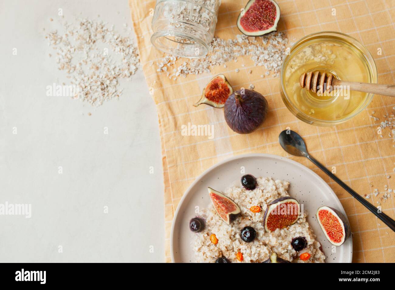 Gesundes Vitaminfrühstück, Haferbrei Haferbrei, Heidelbeeren, frische Feigen und Sanddorn auf gelber Baumwollserviette, Honigstock und langer Löffel, selektiv Stockfoto