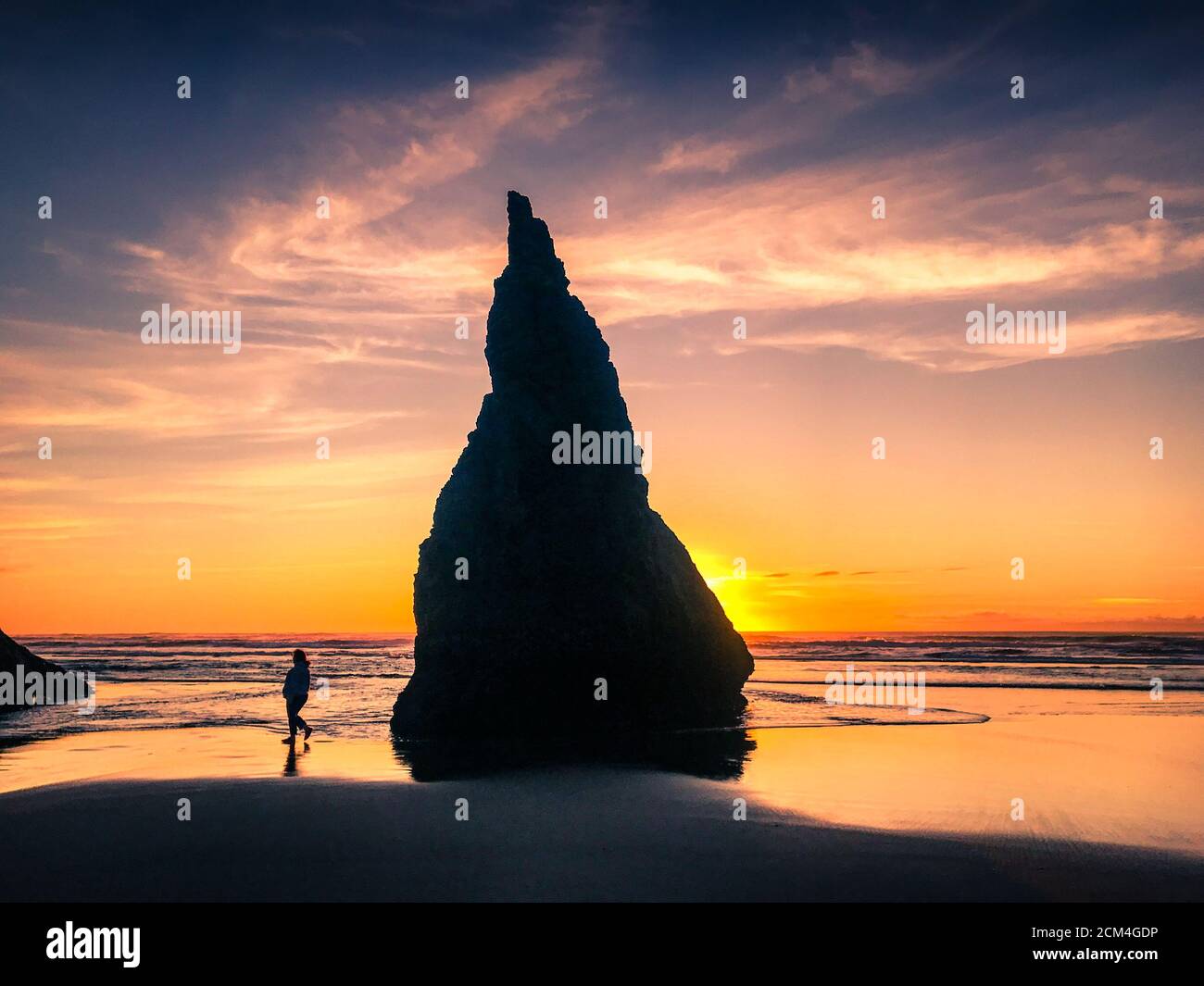 Der Tourist am Oregon Beach spaziert bei Sonnenuntergang am riesigen Meeresstapel vorbei. Stockfoto