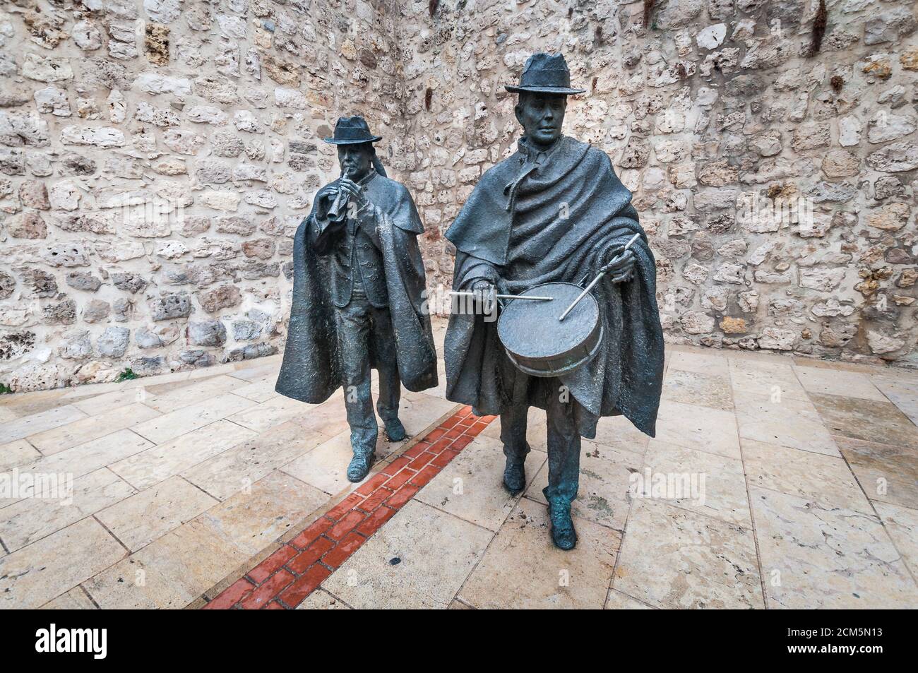 Vorderansicht von Bronzestatuen mit traditionellen Volksmusikern, die vor einer steinigen Wand in einer Straße in Burgos, Spanien, Volksmusik spielen. Stockfoto