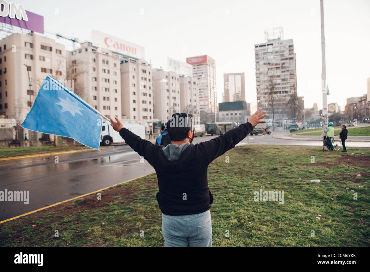 SANTIAGO, CHILE - 11. SEPTEMBER 2020 - EIN Mann protestiert mit einer Flagge mit dem mapuche-Stern 'wüñellfe', während die Polizei die Demonstration unterdrückt. Hundre Stockfoto