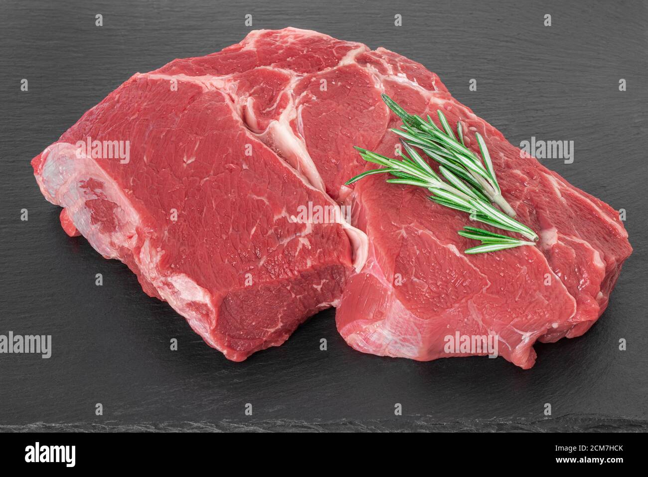 Frisches Stück Rohes Rindfleisch mit Rosmarin auf einem schwarzen Steinbrett Stockfoto