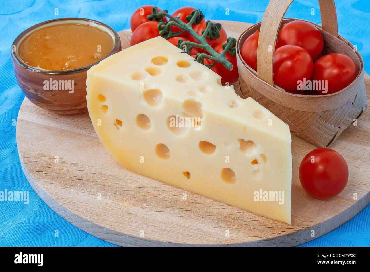 Käseplatte mit Tomaten und Honig dreieckigen Stück Käse serviert Mit Löchern blau Serviette Hintergrund Stockfoto