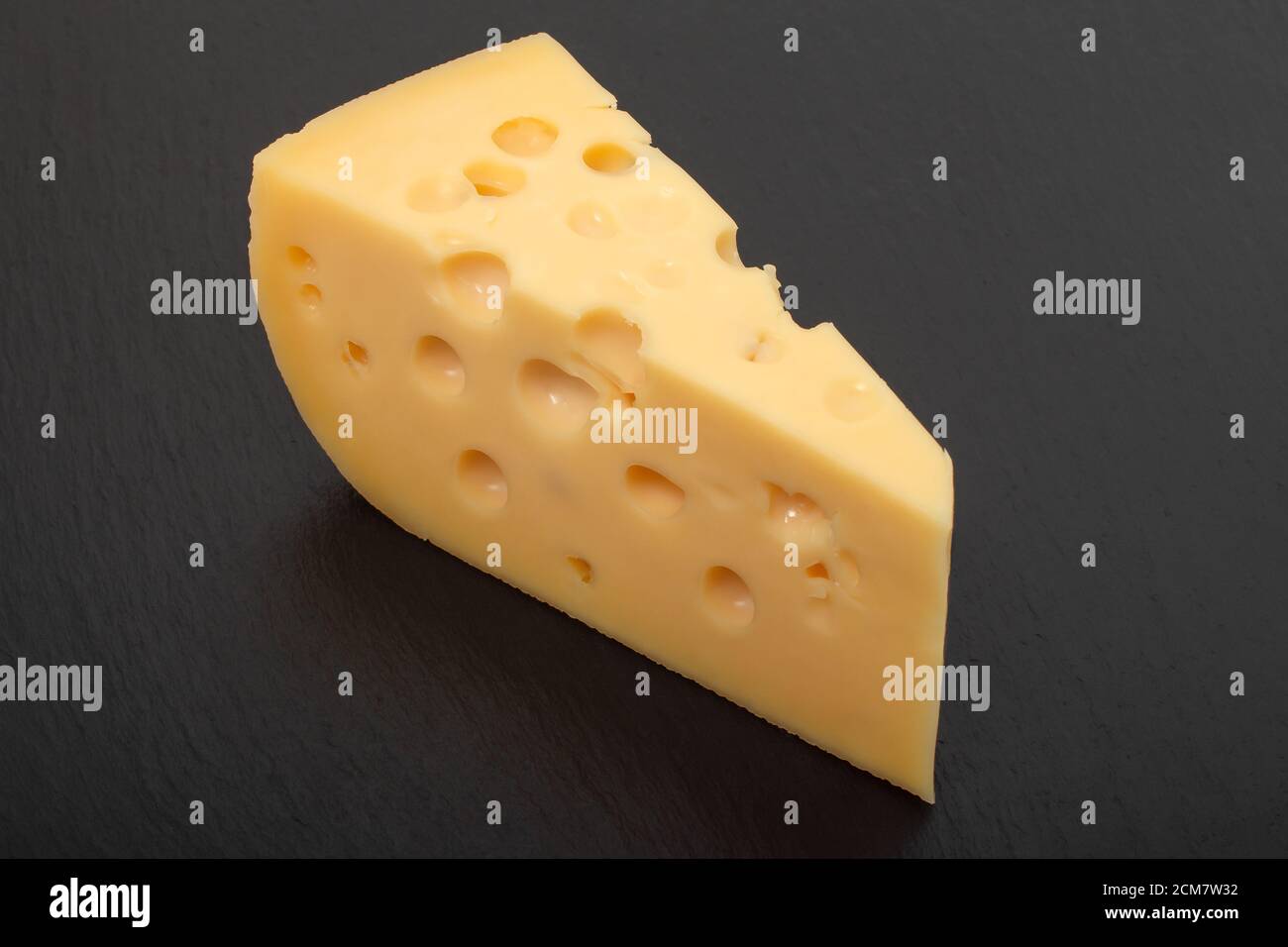 Gelber Maasdam-Käse, dreieckiger Käse mit Löchern, schwarzer Schieferhintergrund aus dunklem Stein Stockfoto