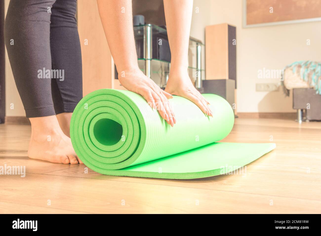 Frau rollt ihre Yogamatte nach einem Training, Yoga online. Ausrüstung für Yoga. Konzept gesunde Lebensweise, Sport und Ernährung. Stockfoto