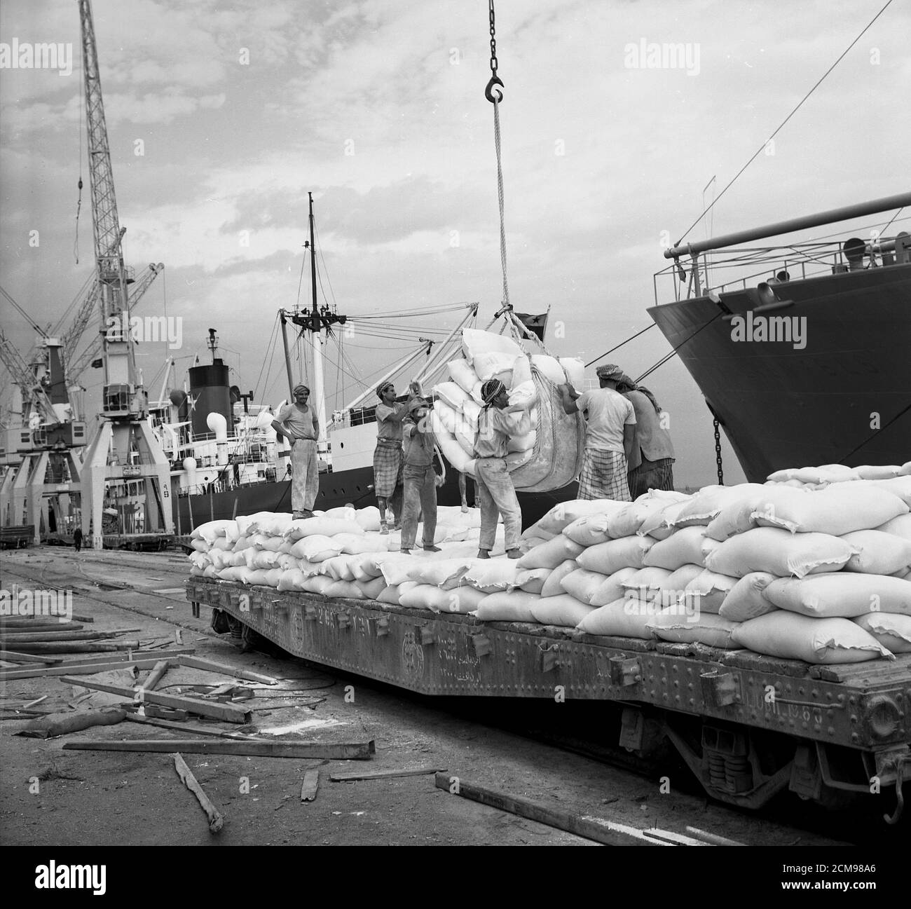 In den 1960er Jahren, historische Hafenarbeiter, die Massengüter von einem Schiff, möglicherweise Lebensmittel wie Getreide, auf einen Tieflader im Hafen von Jeddah, Saudi-Arabien, entladen, Stockfoto