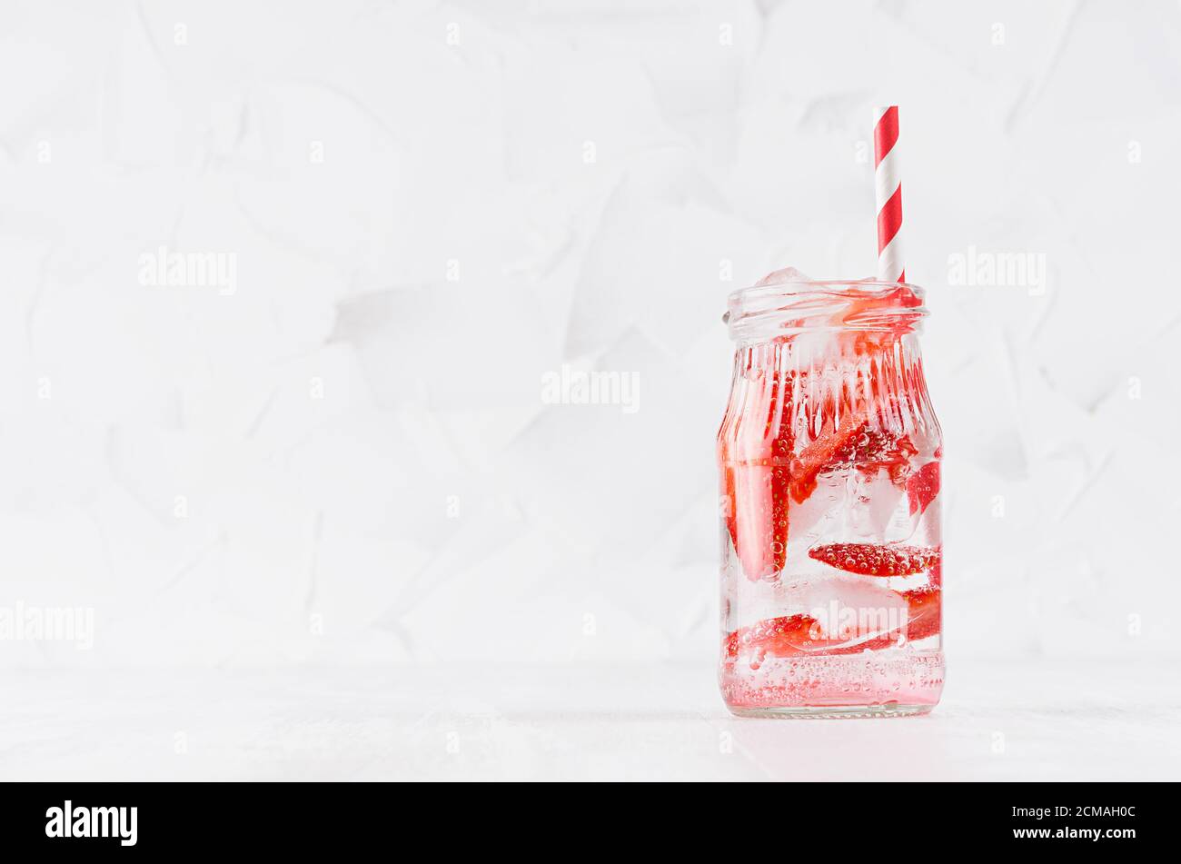 Frische Erdbeerlimonade mit geschnittener Beere, Sodawasser, Eiswürfel mit Stroh im durchsichtigen Glas auf einem weichen hellen weißen Holztisch, Kopierraum. Stockfoto