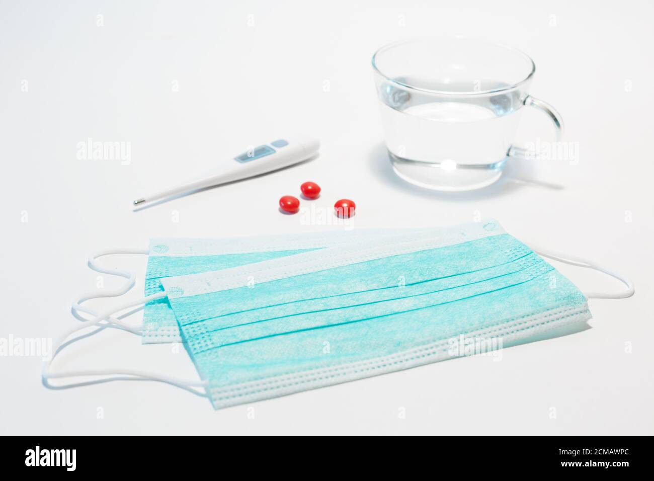 Medizinische Gesichtsschutzmaske, drei rote Tabletten, elektronisches Thermometer zur Messung der Körpertemperatur auf weißem Hintergrund. Medizinische Maske zu verhindern Stockfoto