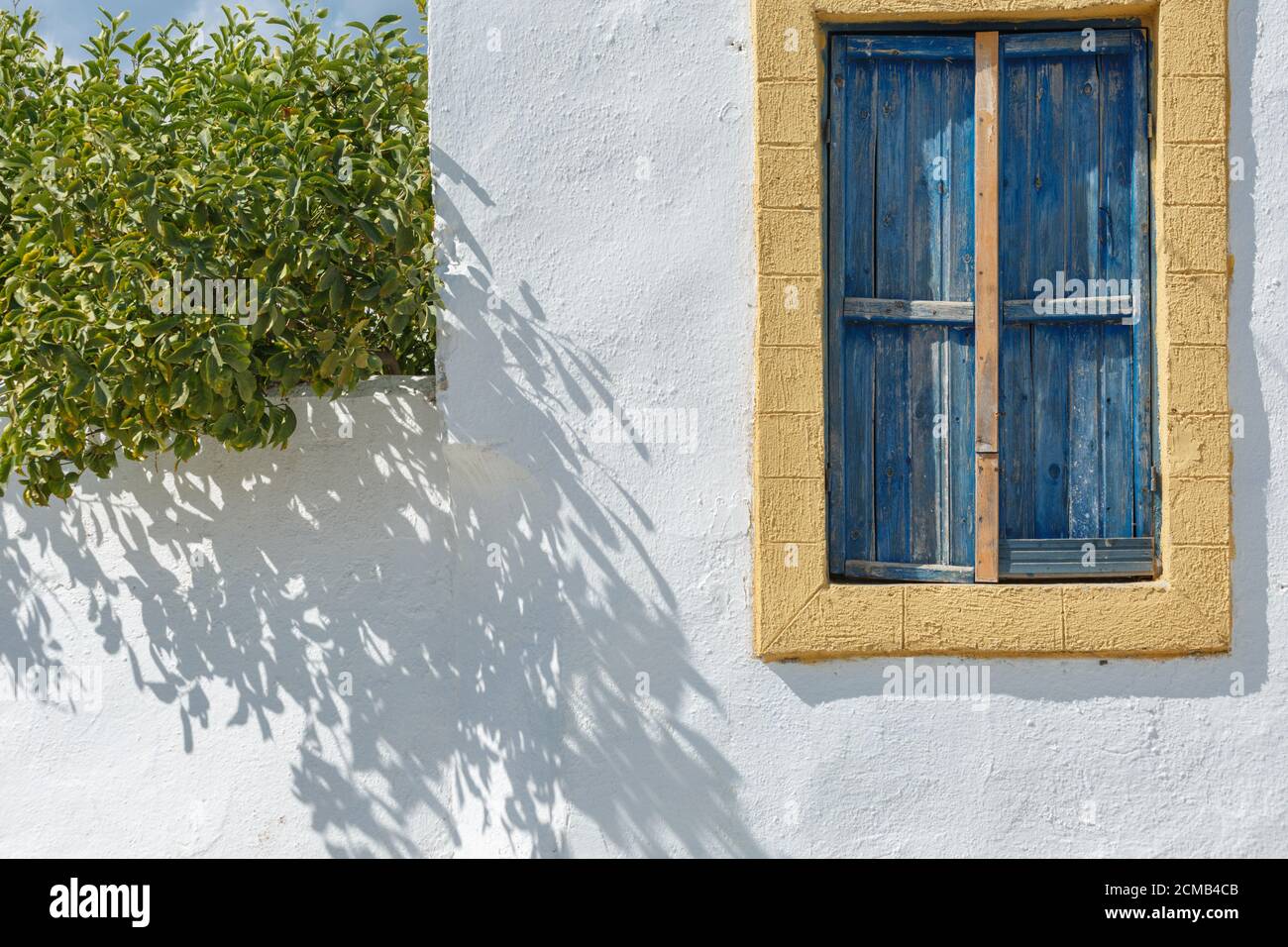 Das Fenster eines griechischen Hauses auf einer weißen Wand Mit gelber Zierleiste und blauen Holzfensterläden auf einem Sunny Tag Stockfoto