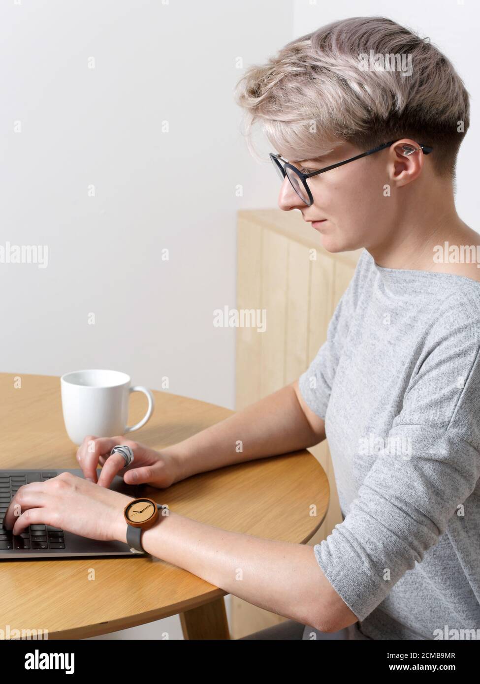 Junge fokussierte Hipster Millennial weiblich mit kurzen blonden Haarschnitt arbeiten mit Laptop in Café-Innenraum, Nahaufnahme Seitenansicht, Blick auf Bildschirm und Typi Stockfoto