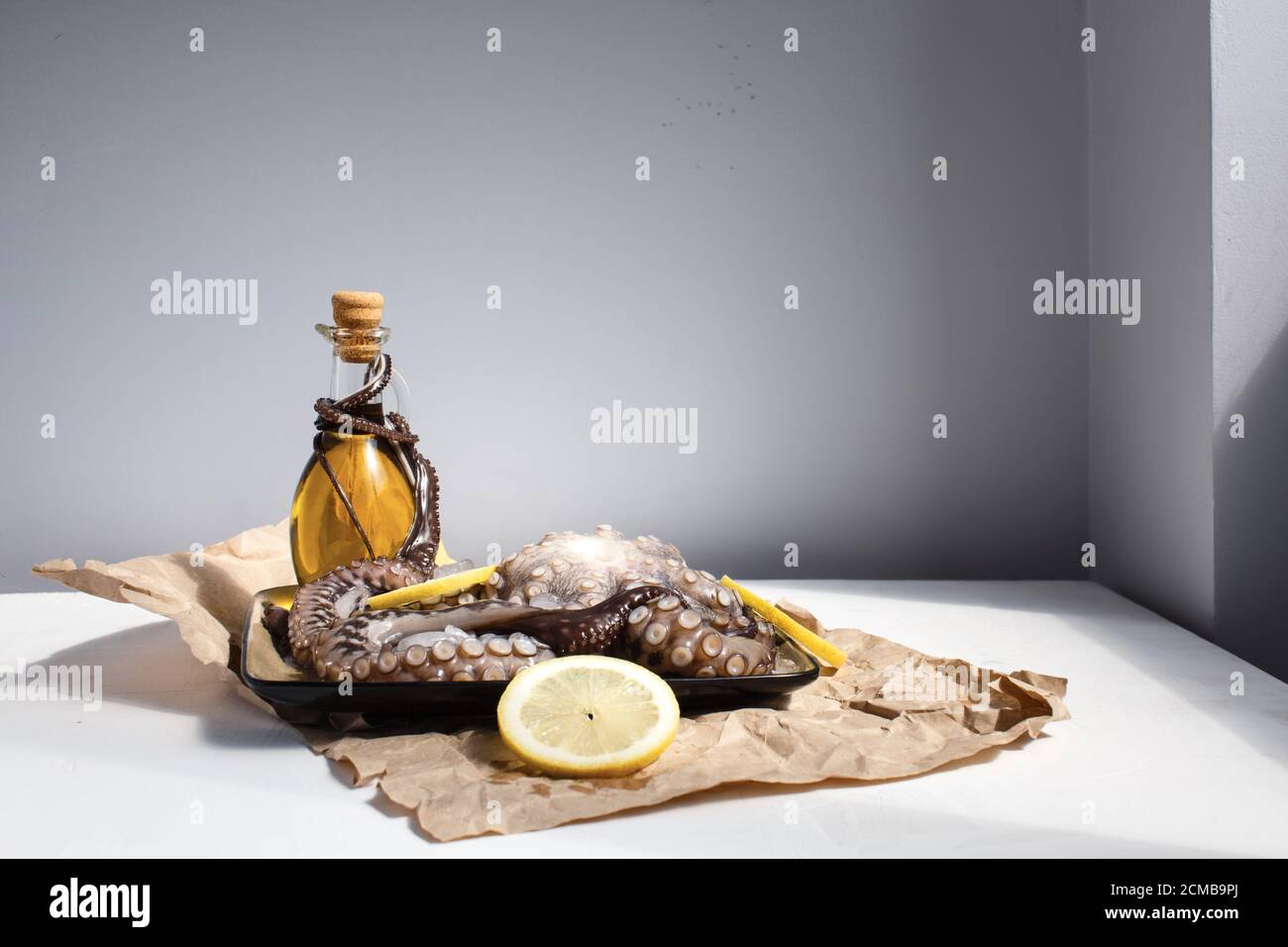 Meeresfrüchte, ganze rohe große Krake auf einem Teller mit Zitronen und Olivenöl bereit für die Vorbereitung, Seitenansicht Stockfoto