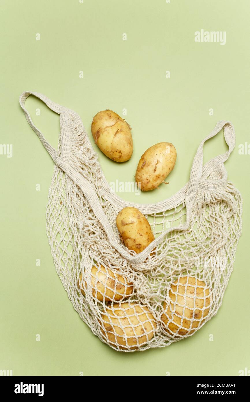 Trendige Saitenbeutel mit frischen jungen Kartoffeln innen auf hellgrünem Hintergrund. Zero Waste nachhaltiges Lifestyle-Konzept. Stockfoto