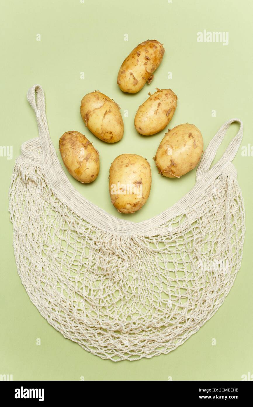 Trendige Saitenbeutel mit frischen jungen Kartoffeln innen auf hellgrünem Hintergrund. Zero Waste nachhaltiges Lifestyle-Konzept. Stockfoto